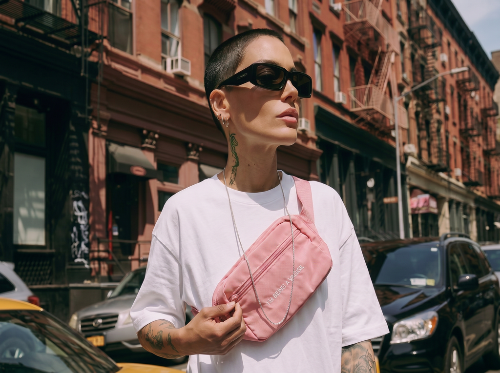 Person wearing a white t-shirt and pink "I'M BEING A  VAGISIL" waist bag on a city street